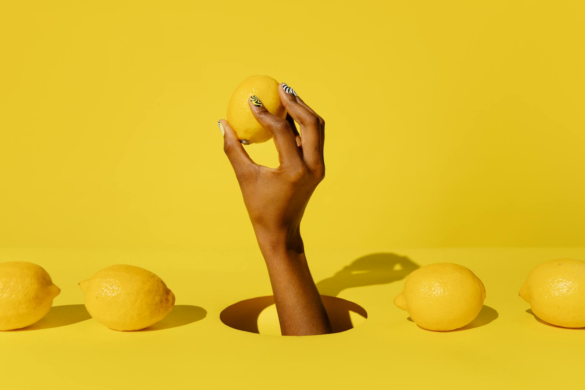 Eine Hand hält einen leuchtend orangefarbenen Vibrator vor einem minimalistischen violetten Hintergrund