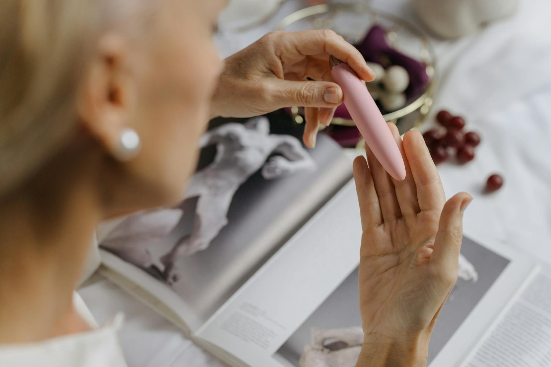 Nahaufnahme einer Frau, die einen rosa Vibrator hält, mit Kunstbüchern im Hintergrund, die intime persönliche Themen betonen