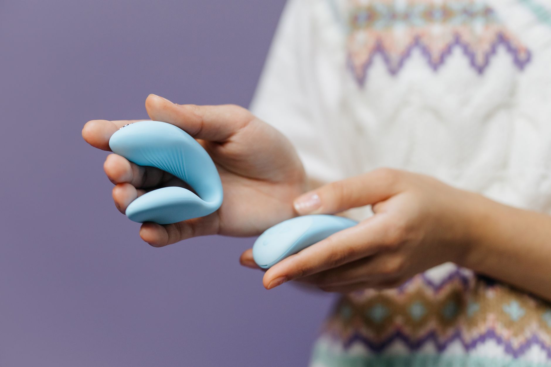 Ein eleganter blauer Vibrator wird in der Hand gegen einen lila Hintergrund gehalten