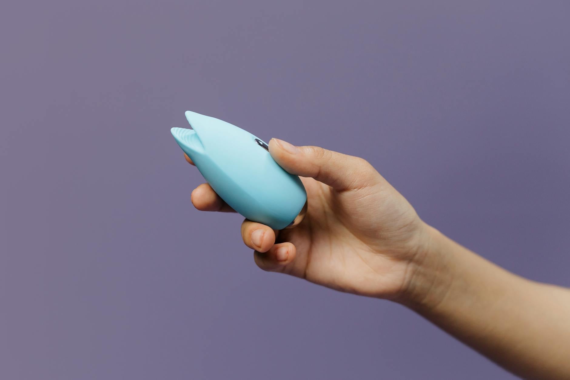 Zwei Hände halten rosa und blaue Silikonvibratoren gegen einen pastellfarbenen Hintergrund