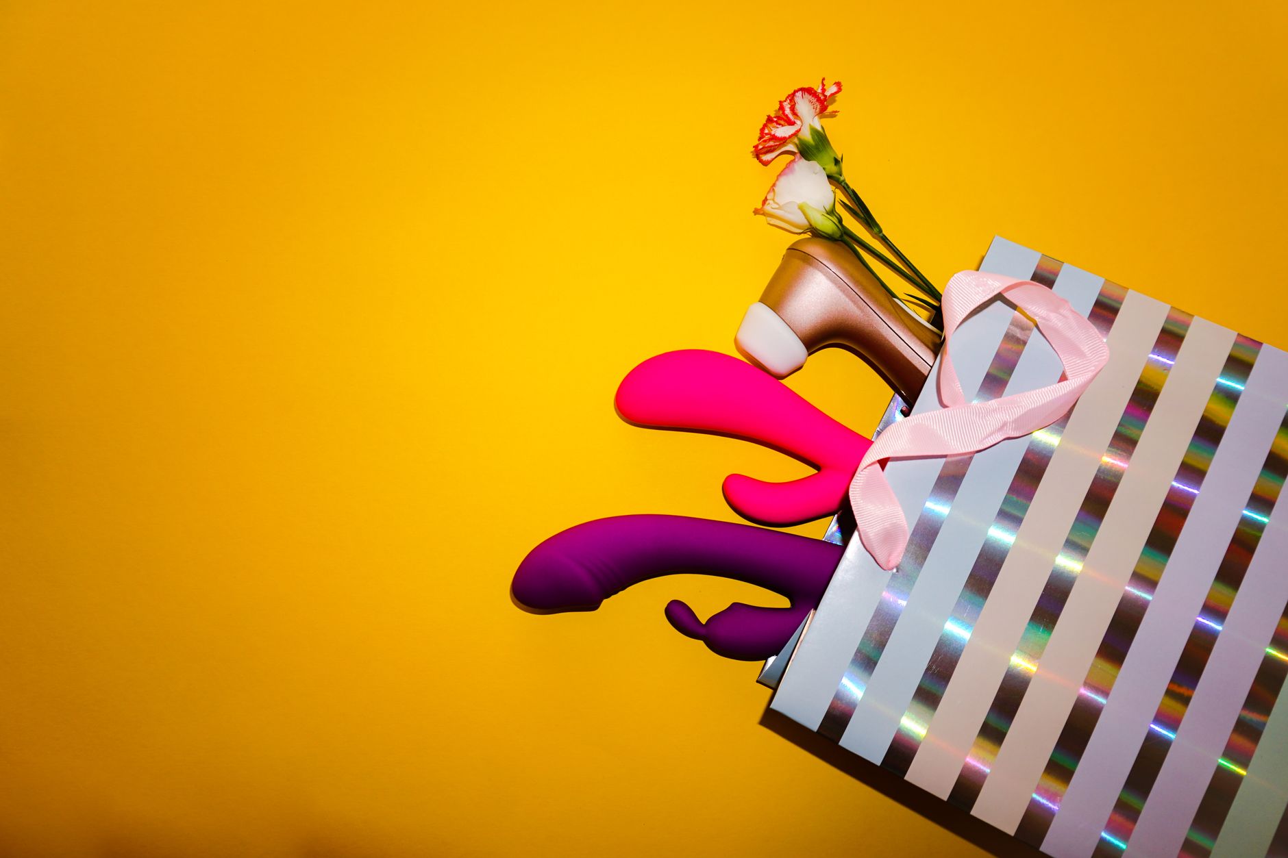 Bunte Vibratoranordnung mit Blumen in einer holografischen Geschenktasche auf gelbem Hintergrund
