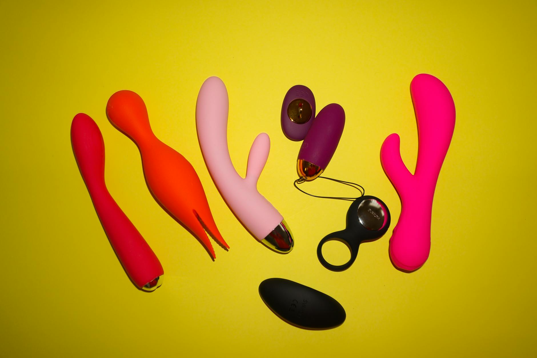 Zwei Hände halten rosa und blaue Vibratoren vor pastellfarbenem Hintergrund