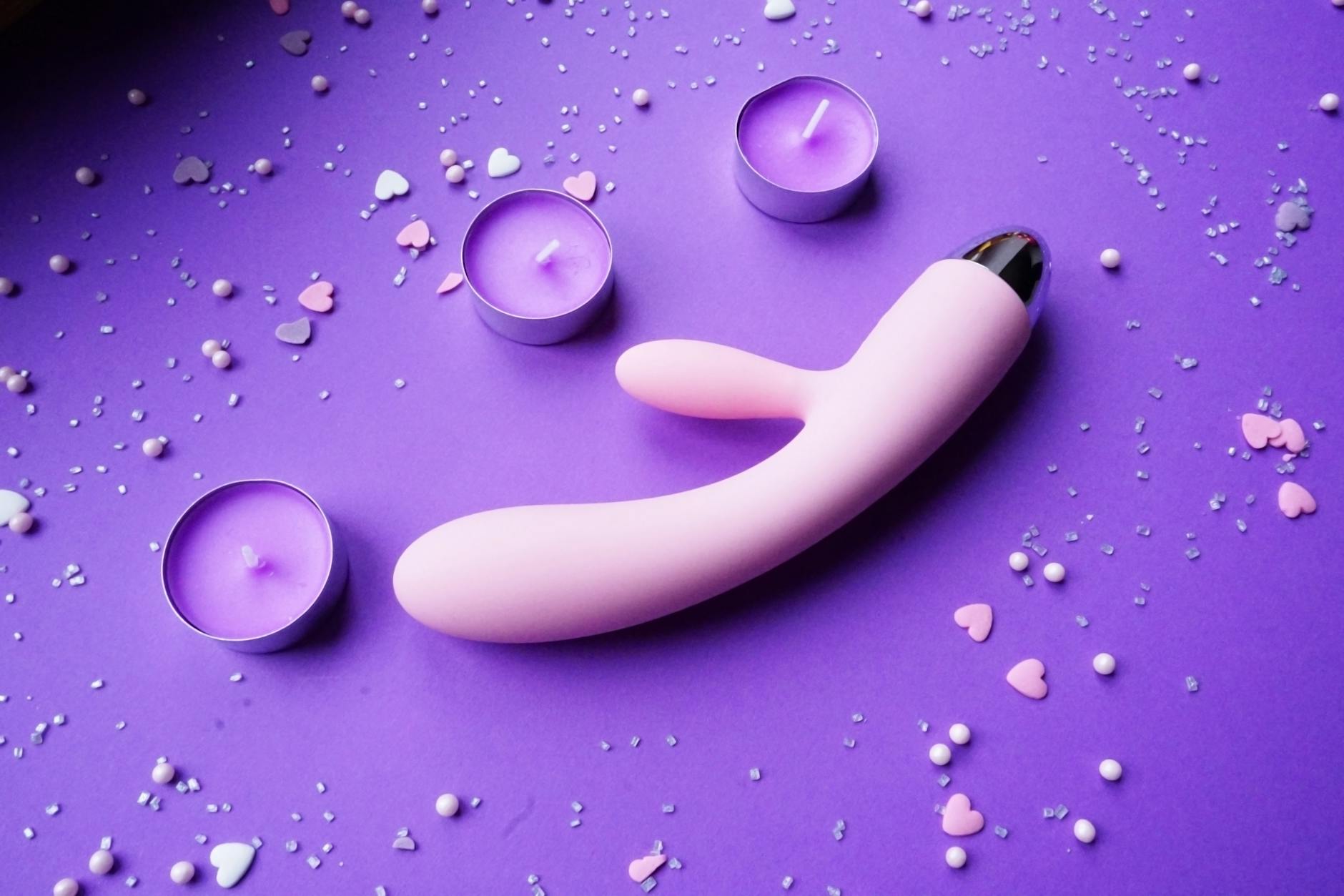Rosa Vibrator auf violettem Hintergrund mit Herzconfetti und Kerzen für romantische Stimmung